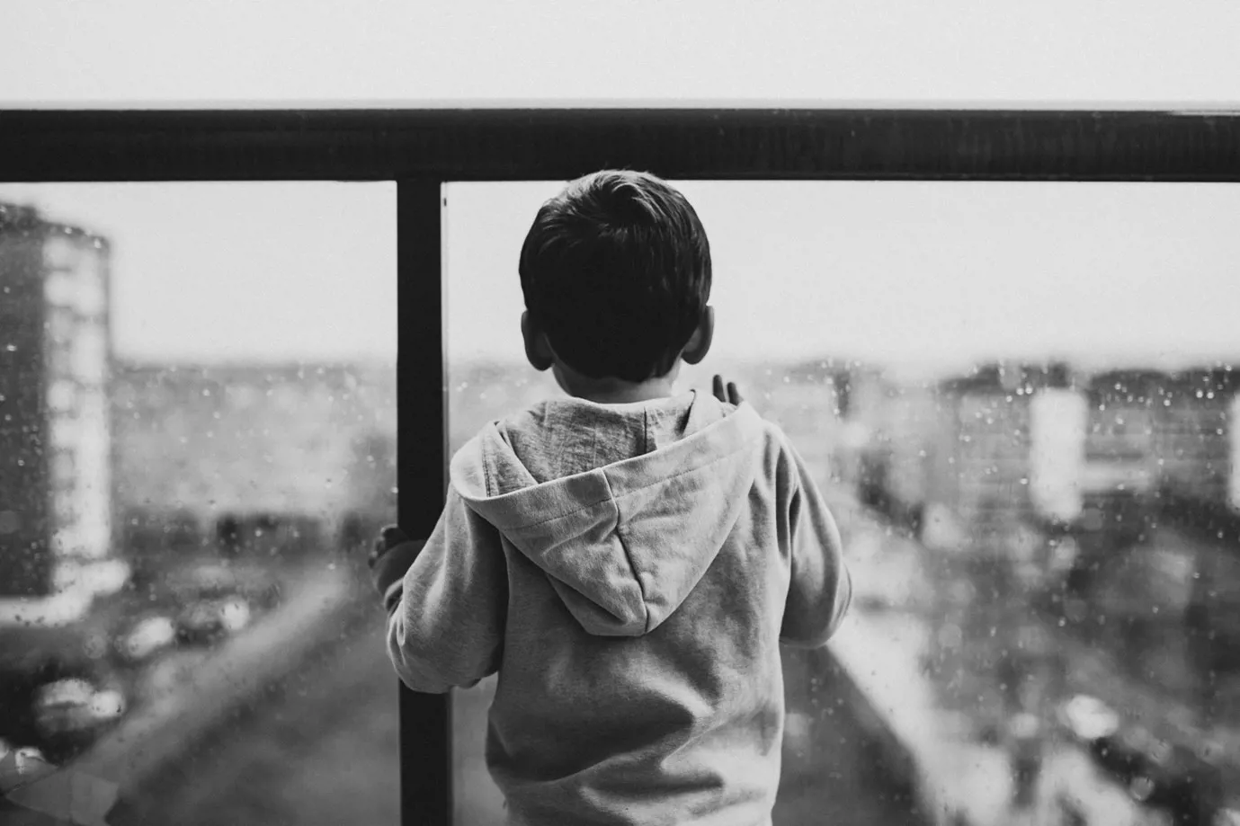 a black and white image of a young boy on a balcony overlooking a city