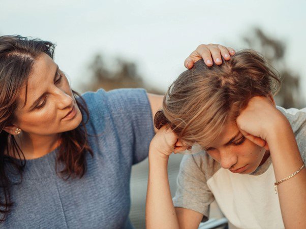 A young boy looking sad, being comforted by parent