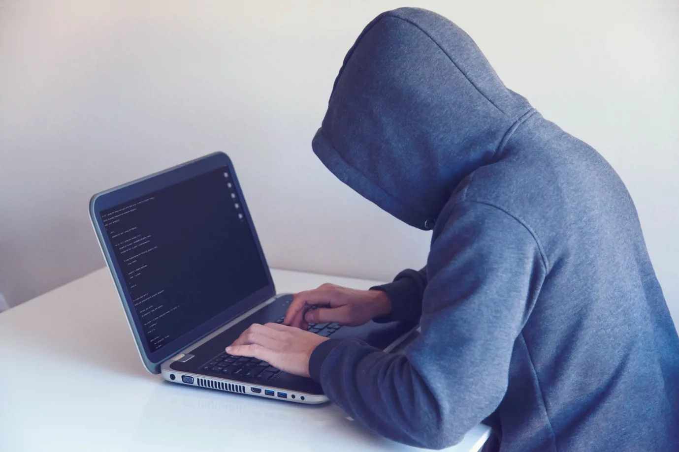 Suspicious person in a hood typing on a laptop