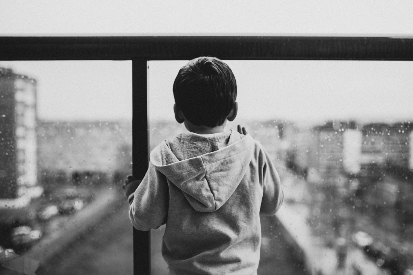 a black and white image of a young boy on a balcony overlooking a city