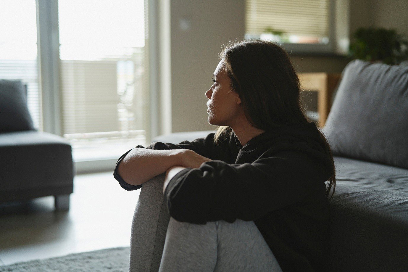 woman sat up against sofa looking sad