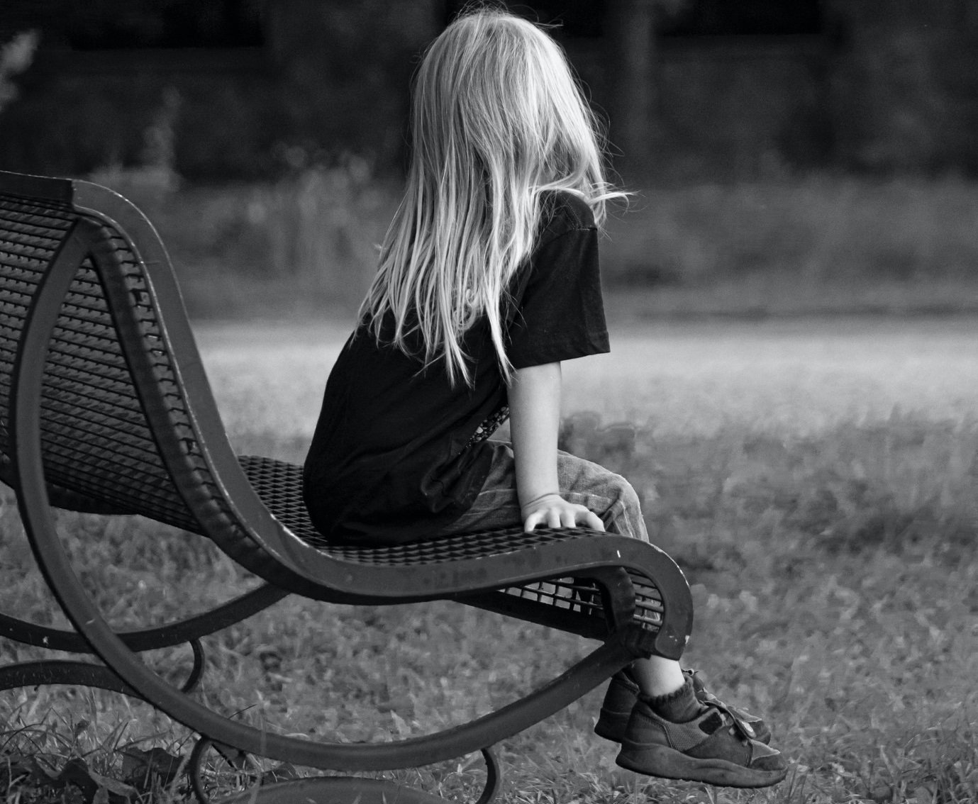 a black and white picture of a young girl sat on a public bench