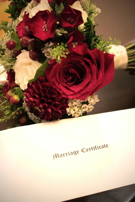 A bouquet of roses behind a card saying 'Marriage Certificate'