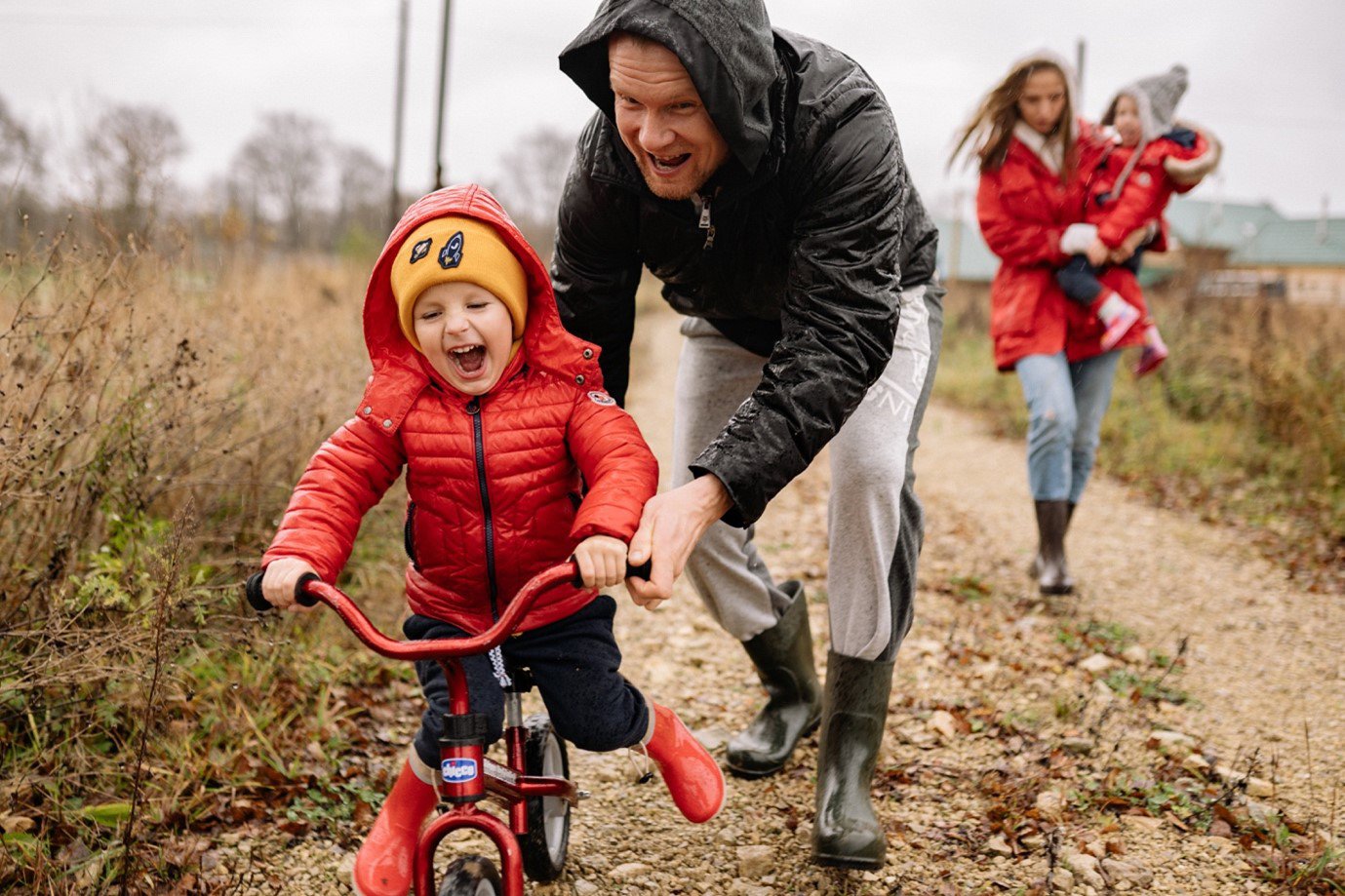 Parents playing with their children, dad pushing child on a bike in foreground