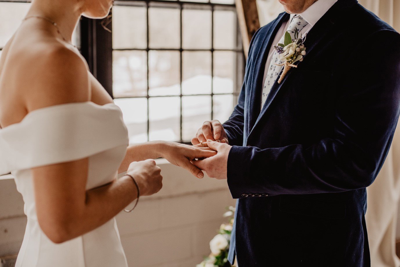 A couple getting married. The man is placing a ring on the woman's finger