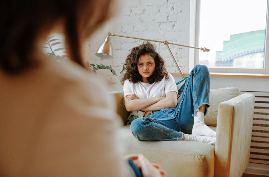 A young girl cross-armed sat on a sofa