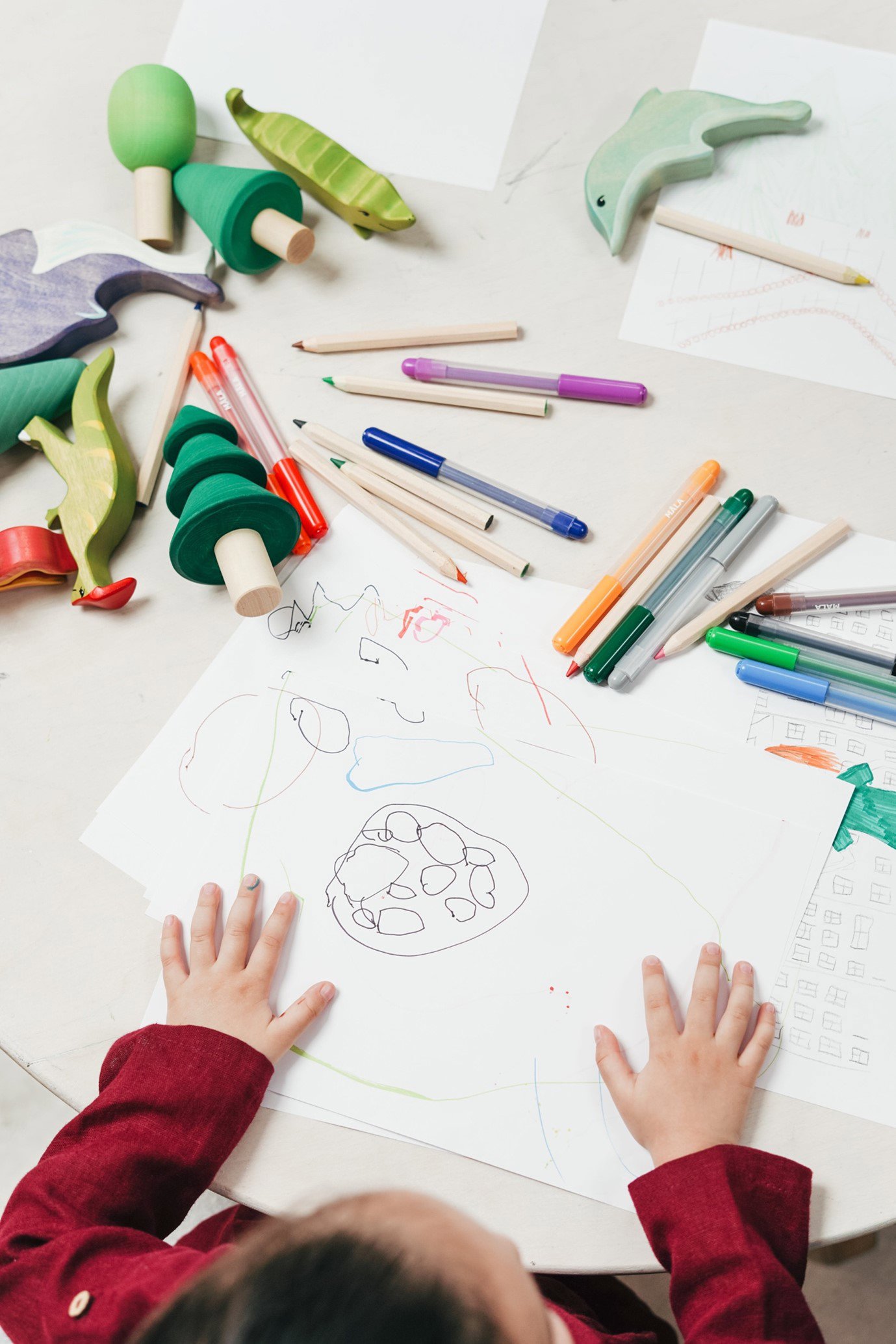 child drawing picture with crayons on desk